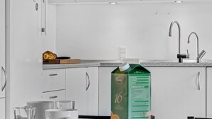 Une cuisine moderne avec des meubles blancs, un plan de travail et un carton vert de jus d’orange.