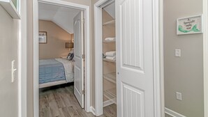 A bedroom with a bed, a nightstand, and a wall-mounted shelf with folded towels. - “Mermaid’s Dream” Short Walk from the Waves & Pool (Myrtle Beach)