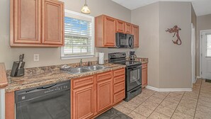 A kitchen with wooden cabinets, a microwave, an oven, a dishwasher, and a granite countertop. - “Mermaid’s Dream” Short Walk from the Waves & Pool (Myrtle Beach)