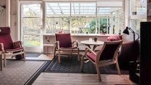 Ein Wintergarten mit großen Fenstern, Holzboden und mehreren Stühlen sowie einem Tisch.