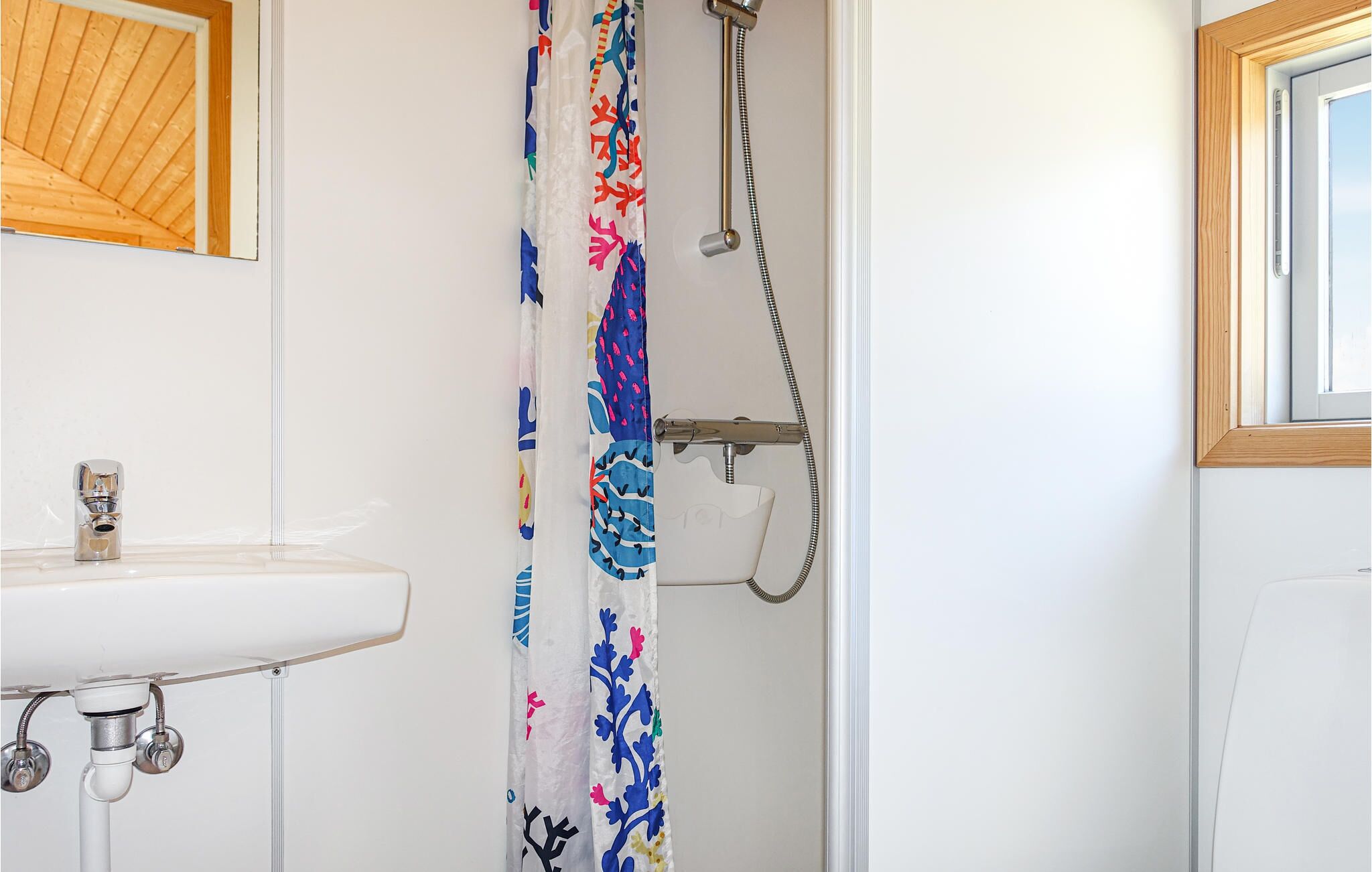 Un bagno con un lavandino bianco, una doccia con tenda colorata e un soffitto in legno.