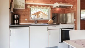 Una cucina compatta con pareti in legno, un lavello, un fornello Bosch e una finestra che si affaccia su una struttura in legno.