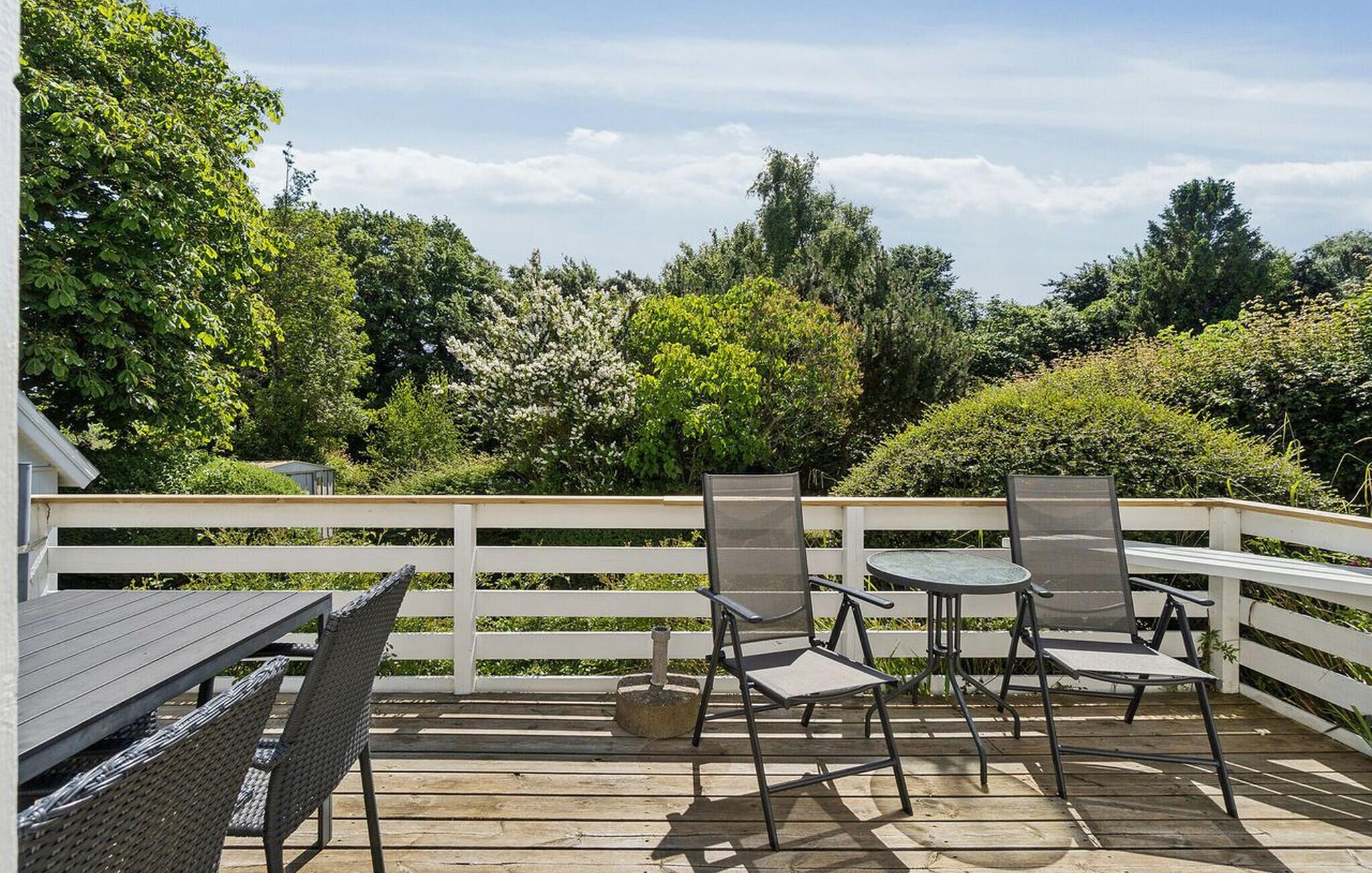 Une terrasse extérieure avec une table et des chaises, entourée d’une clôture blanche et d’une végétation luxuriante.