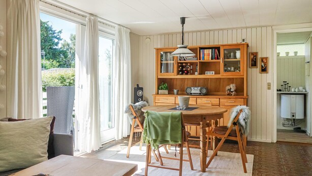 En mysig matplats med ett träbord och stolar, en grön duk och en bokhylla fylld med böcker och dekorativa föremål.