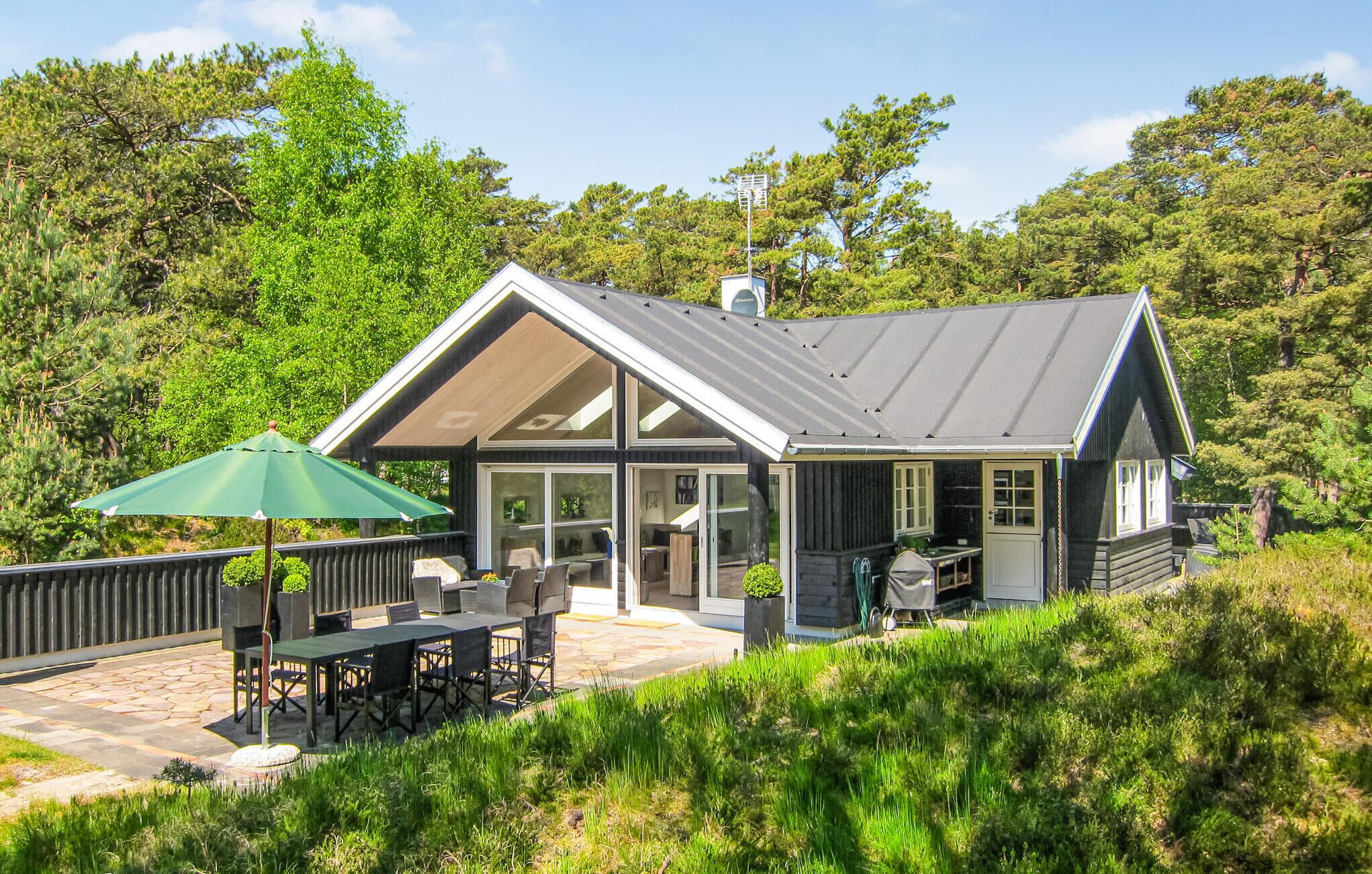 Una cabaña moderna con un amplio patio, mobiliario exterior y una zona cubierta.