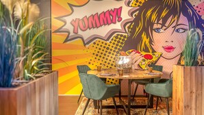 A dining area with a round wooden table, green upholstered chairs, and a vibrant pop art mural in the background. - luxurioese Ferienwohnung (Matrei in Osttirol)