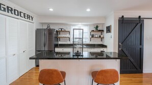 A modern kitchen with a central island, two bar stools, a refrigerator, and a sliding barn-style door.