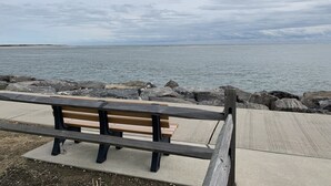 A bench at a rocky waterfront with a view of the sea.
