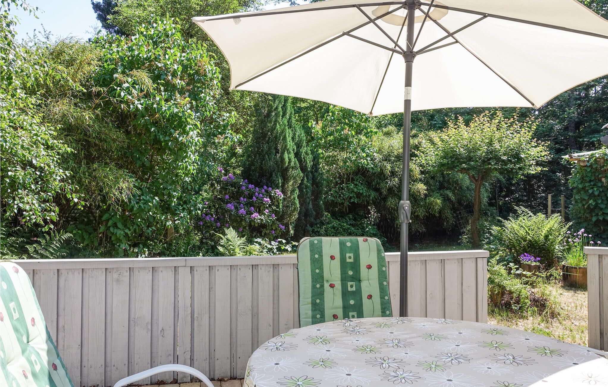 Een terras met een tafel, stoelen en een parasol, omgeven door een houten hek.