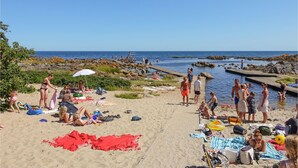 A beach scene with people sunbathing, swimming, and walking along the shore. - 5 bedroom nice home in Svaneke (Svaneke)