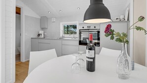 Et moderne køkken med hvide skabe, en indbygget ovn og et spiseområde med et bord dækket til to.