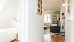 A narrow hallway with a bed on the left, a black chair in the center, and a bookshelf on the right. - Stunning apartment in Gudhjem with WiFi (Gudhjem)
