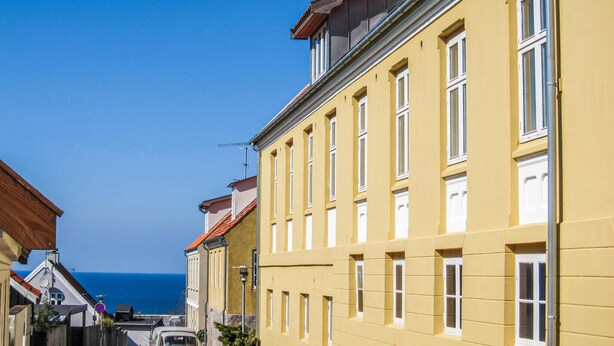 A yellow building with multiple windows and a balcony, located in a coastal area with a clear view of the sea. - Stunning apartment in Gudhjem with WiFi (Gudhjem)