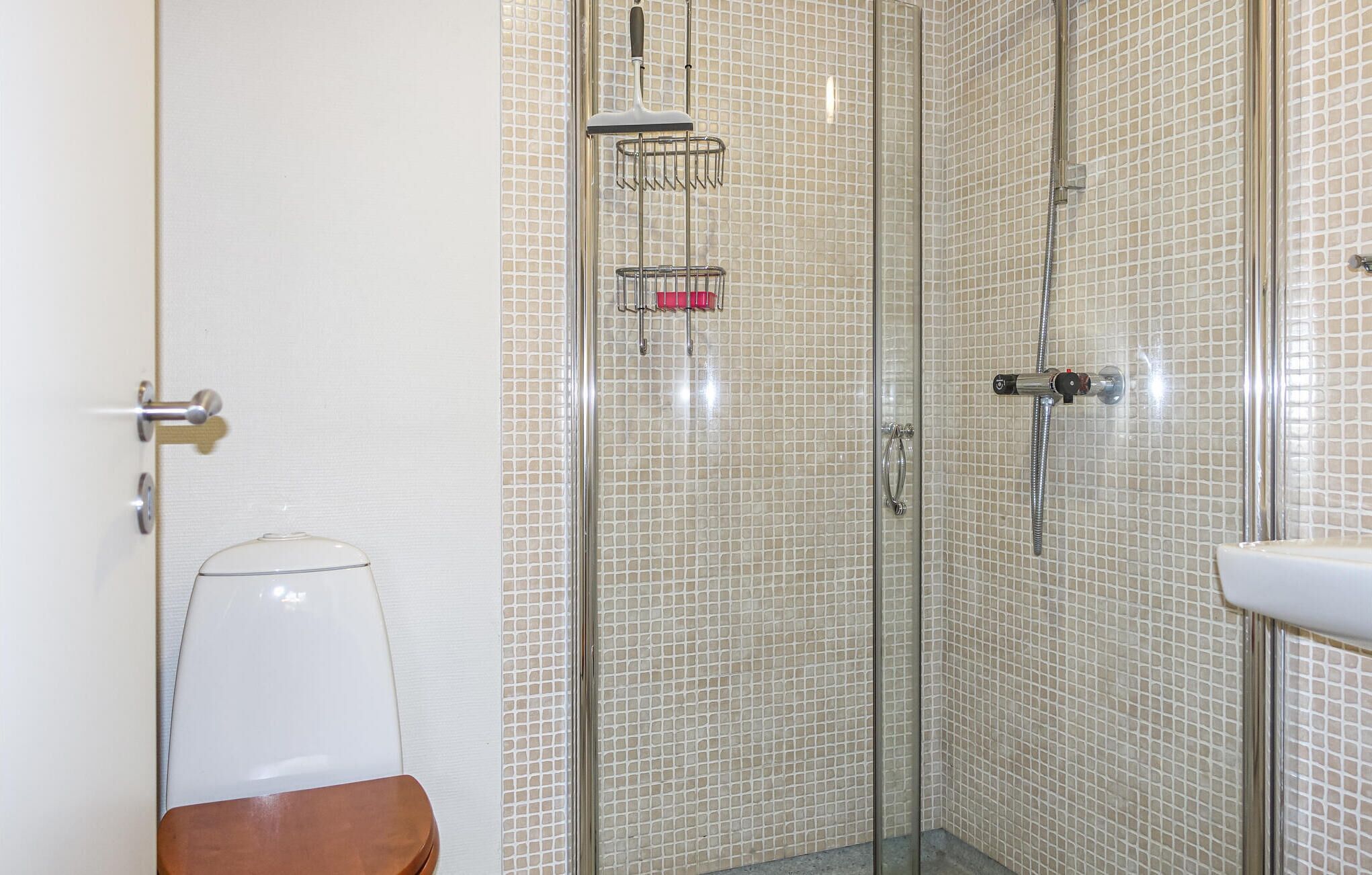 Ein Badezimmer mit Duschkabine aus Glas, einem weißen Waschbecken und einer Holzbank.