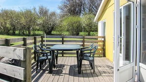 A wooden deck with a table and chairs, a wooden fence, and a yellow building with a glass door. - 1 bedroom cozy home in Allinge (Allinge)