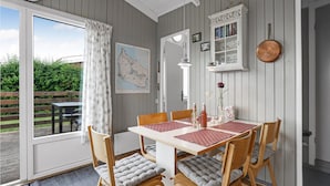A dining area with a table set for four, wooden chairs with cushioned seats, a map on the wall, and a cabinet with books and decorative items. - 1 bedroom cozy home in Allinge (Allinge)