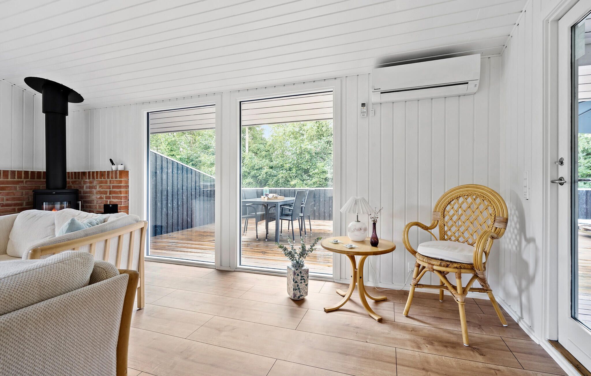A cozy room with a fireplace, a wicker chair, a small table with a vase, and a sliding glass door leading to an outdoor deck.