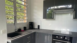 A modern kitchen with grey cabinets, a stainless steel range hood, a built-in oven, and a window with blinds. - Elegant, recently renovated apartment (Sainte-Anne)