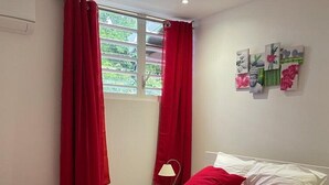 A bedroom with a bed, red curtains, a window, a wall-mounted picture frame, and a bedside lamp. - Elegant, recently renovated apartment (Sainte-Anne)