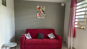 A red sofa with patterned cushions, a small round table, and a wall-mounted painting. - Elegant, recently renovated apartment (Sainte-Anne)