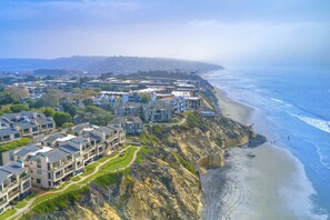 A coastal residential area with modern buildings, a beach, and a cliffside.