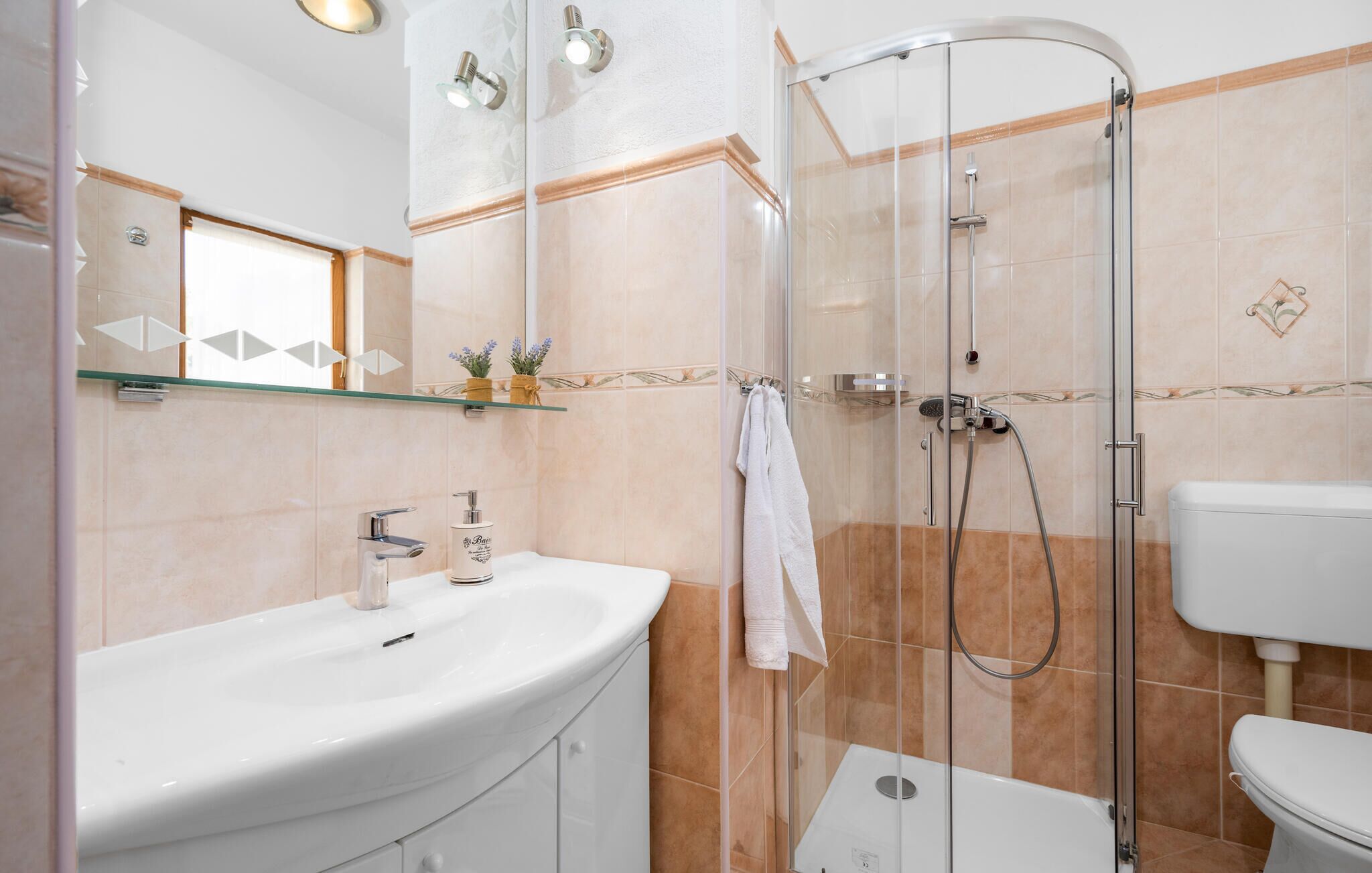 Un bany modern amb plat de dutxa envoltat de vidre, un lavabo blanc i un vàter.