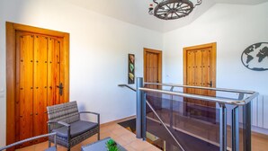 A modern interior with wooden doors, a wicker chair, a glass table, and a staircase with a glass railing. - Stunning home in Cehegín (Cehegín)