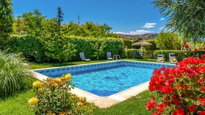 A rectangular swimming pool with a clear blue water surface, surrounded by lush greenery and red flowers. - Stunning home in Cehegín (Cehegín)