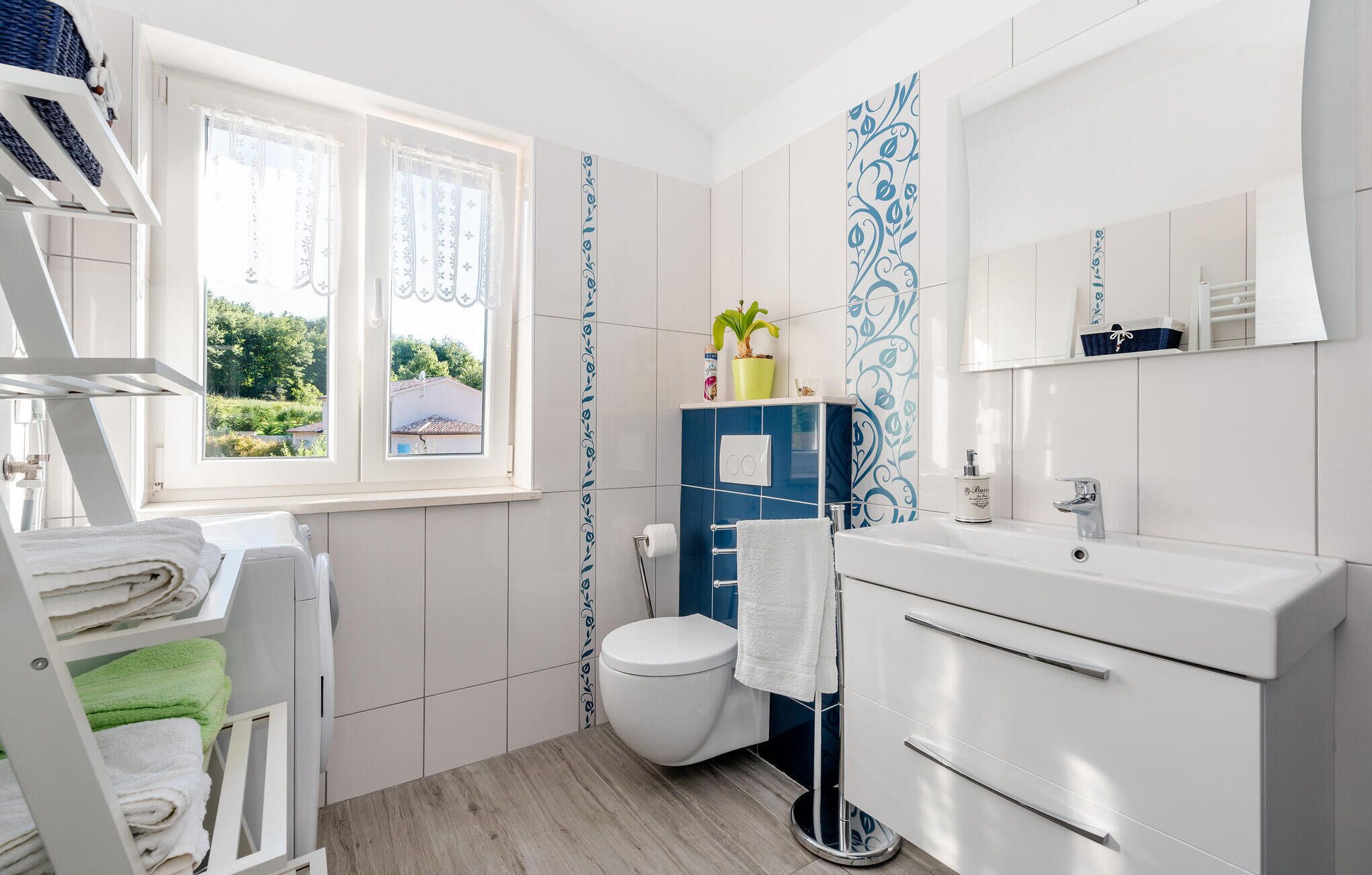 A modern bathroom with a toilet, sink, and towel rack. There is a window with curtains, a plant on the sink, and a mirror above the sink.