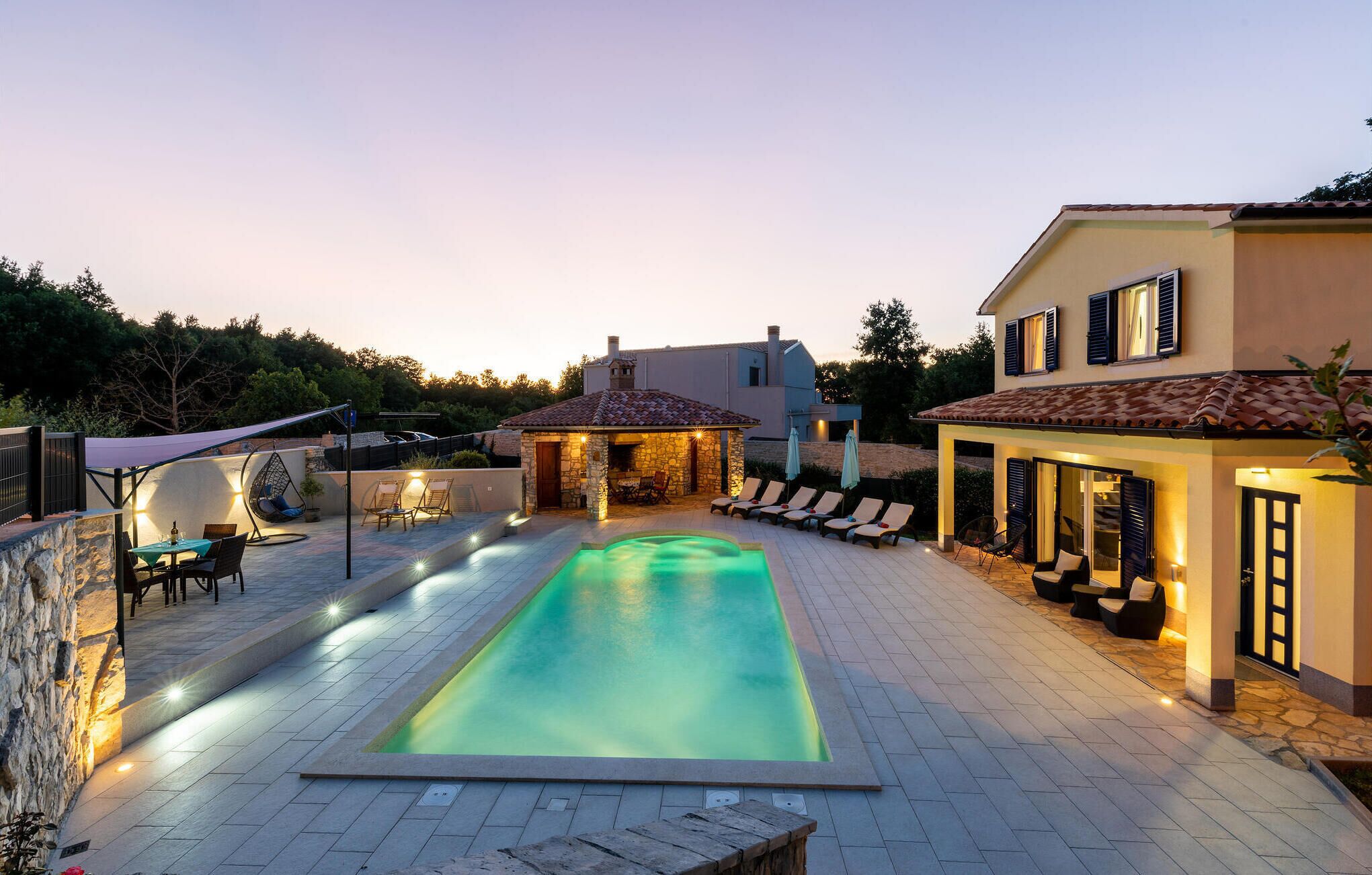 A swimming pool with a stone deck, lounge chairs, and a stone patio area.