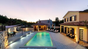 Une piscine avec une terrasse en pierre, des chaises longues et un espace patio également en pierre.