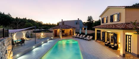 A swimming pool with a stone deck, lounge chairs, and a stone patio area.