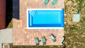 An aerial view of a rectangular swimming pool with a tiled deck, surrounded by lounge chairs and a small garden area. - Awesome home in Mirkopolje (Mirkopolje)