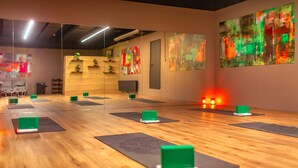 A yoga studio with wooden floors, green yoga blocks, and abstract paintings on the walls.