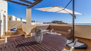 Eine Dachterrasse mit einem runden Holztisch, Korbmöbeln und einem großen Sonnenschirm.