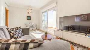 Ein modernes Wohnzimmer mit einer Couch, einem Fernseher und einem Essbereich mit Tisch und Stühlen.