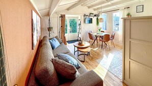 Un salon chaleureux avec un canapé, un coin repas avec une table et des chaises, et une cuisine visible au fond.