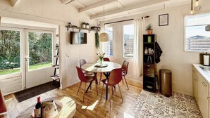 Un coin repas avec une table ronde, des chaises rouges, un téléviseur fixé au mur et une vue sur la verdure à l’extérieur.
