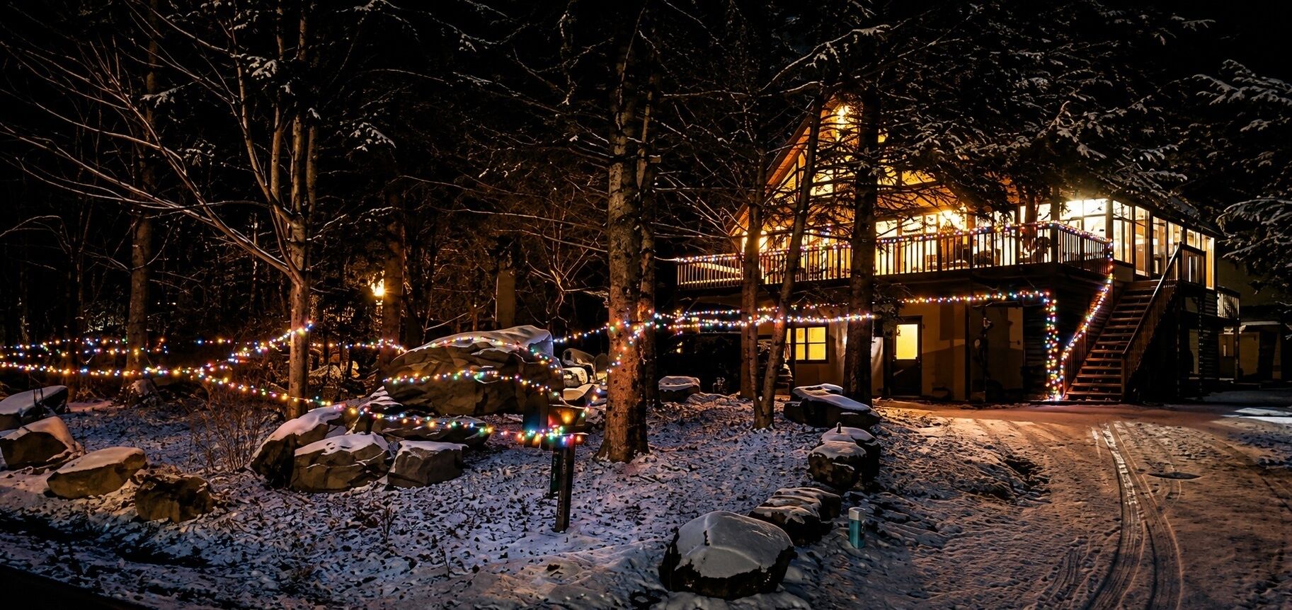 A snow-covered landscape with a wooden cabin illuminated by string lights, surrounded by trees.