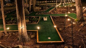 En minigolfbane med flere baner, omgivet af træer og oplyst af lyskæder.