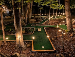 En minigolfbana med flera banor, omgiven av träd och upplyst av ljusslingor.