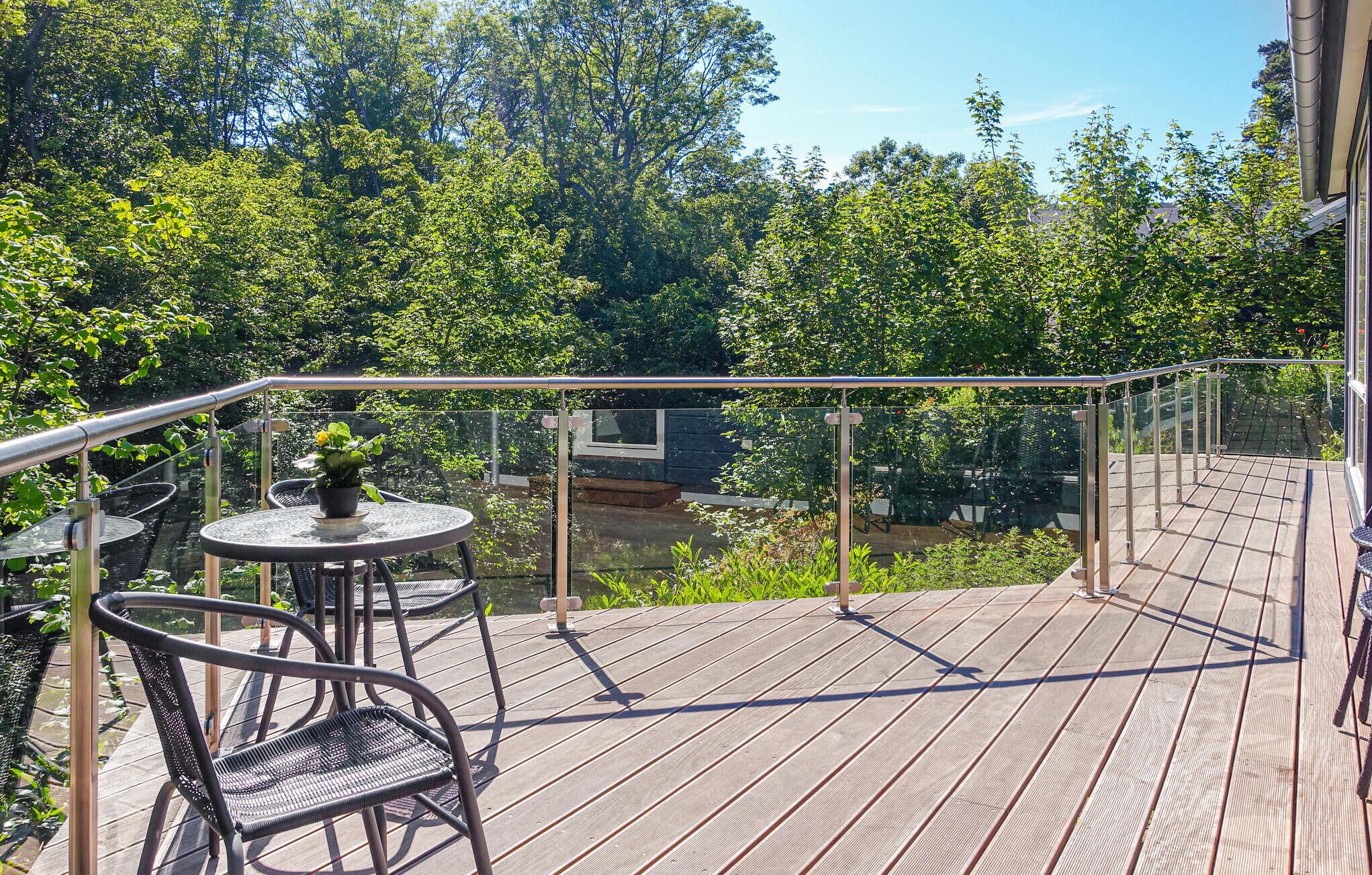 A wooden deck with metal railings, a round table with chairs, and a potted plant.