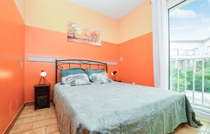 A bedroom with a bed, a nightstand, a lamp, and a window with a view of greenery.