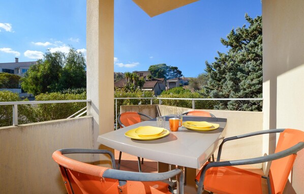 A balcony with a table set for two, chairs, and a view of houses and trees.