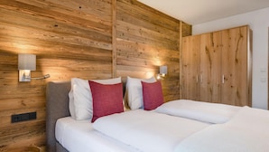 A bedroom with a wooden headboard, a bed with white bedding and red pillows, a bedside table, and a wardrobe. - hochwertige Ferienwohnung (Matrei in Osttirol)