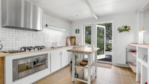 Een moderne keuken met witte kastjes, een roestvrijstalen afzuigkap, een inbouwoven en een groot raam dat voor natuurlijk licht zorgt.