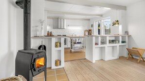 Een moderne keuken met een houtkachel, witte kasten en uitzicht op de eethoek.
