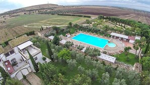 Vista aérea de un complejo turístico con una amplia piscina, rodeado de exuberante vegetación y algunos edificios.