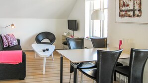 A modern living room with a dining area, featuring a white sofa, black chairs, a white table, and a large window with natural light. - Cozy apartment in Gudhjem with WiFi (Gudhjem)