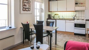 A compact kitchen with white cabinets, a microwave, a coffee maker, and a stove. There is a dining area with a table and chairs, and a window with curtains. - Cozy apartment in Gudhjem with WiFi (Gudhjem)